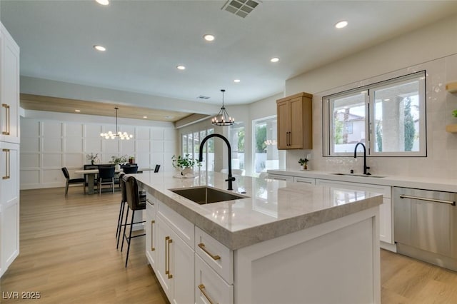 kitchen with sink, white cabinetry, a center island with sink, dishwasher, and light stone countertops