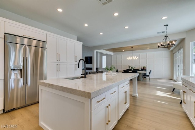 kitchen with sink, built in refrigerator, hanging light fixtures, an island with sink, and white cabinets