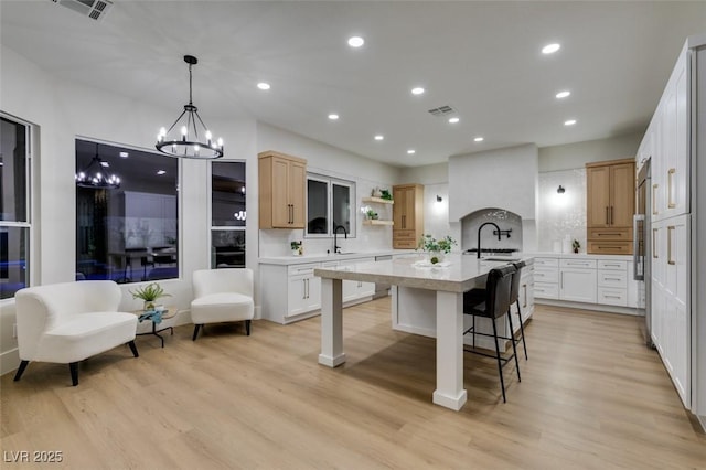 kitchen featuring white cabinetry, sink, decorative backsplash, a kitchen island with sink, and light hardwood / wood-style floors