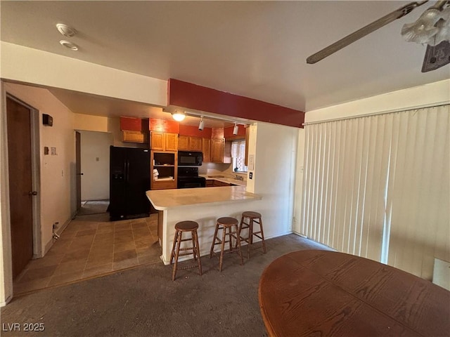 kitchen with a breakfast bar area, black appliances, kitchen peninsula, and carpet