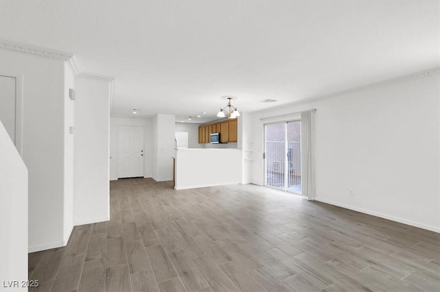 unfurnished living room with crown molding, an inviting chandelier, and light wood-type flooring