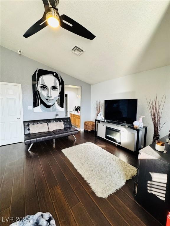 living room with ceiling fan, lofted ceiling, dark wood-type flooring, and a textured ceiling