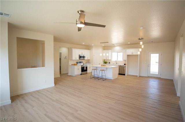 kitchen featuring a center island, stainless steel appliances, light countertops, a kitchen bar, and white cabinetry