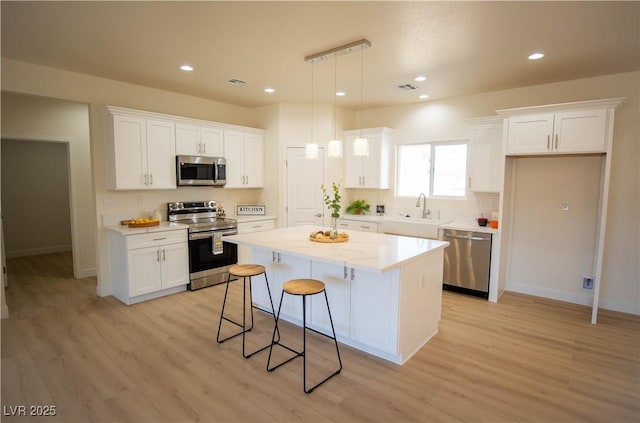 kitchen with appliances with stainless steel finishes, white cabinets, a kitchen island, and a sink