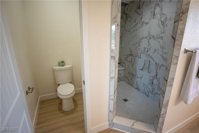 bathroom with toilet, a marble finish shower, baseboards, and wood finished floors