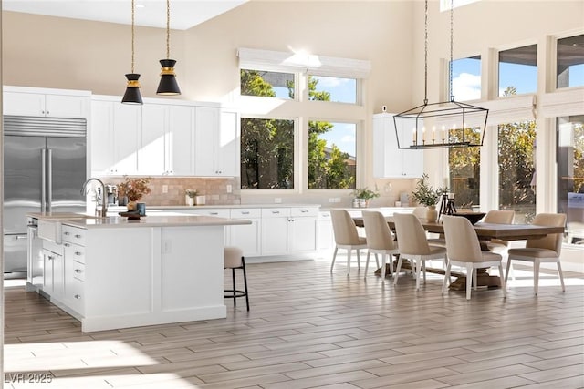 kitchen with a kitchen island with sink, pendant lighting, white cabinets, and built in refrigerator