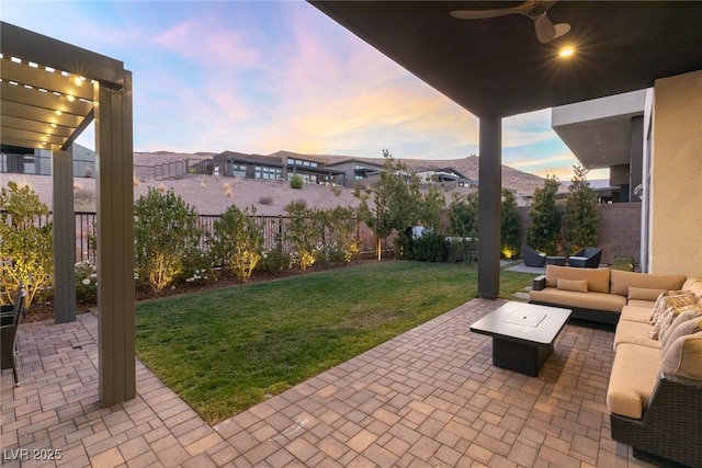 patio terrace at dusk featuring an outdoor hangout area, ceiling fan, and a lawn