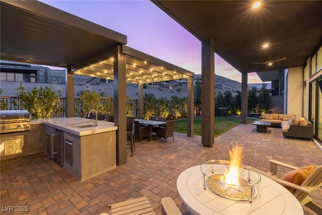 patio terrace at dusk with sink, area for grilling, grilling area, a mountain view, and an outdoor living space with a fire pit