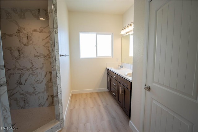 bathroom with wood finished floors, baseboards, a marble finish shower, double vanity, and a sink