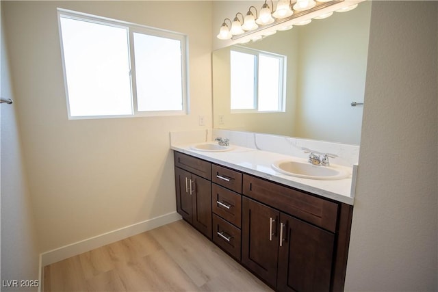 full bath with double vanity, wood finished floors, baseboards, and a sink