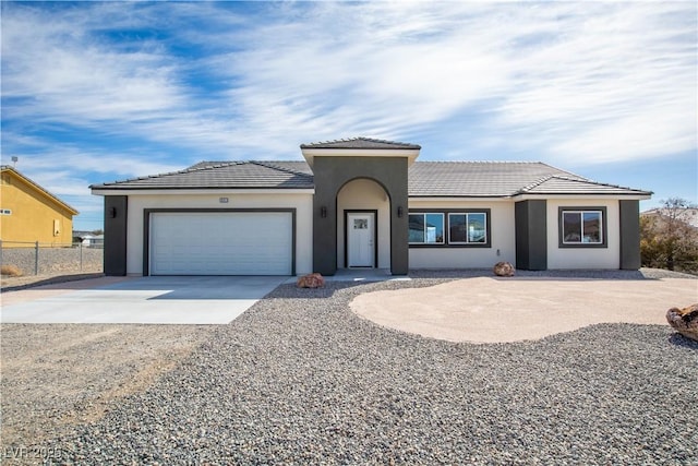 view of front facade with fence, a tile roof, stucco siding, a garage, and driveway