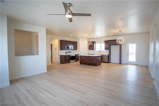 kitchen featuring dark brown cabinets, a kitchen island, open floor plan, stainless steel appliances, and a sink