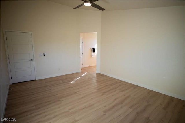 spare room with light wood-type flooring, a high ceiling, ceiling fan, and baseboards