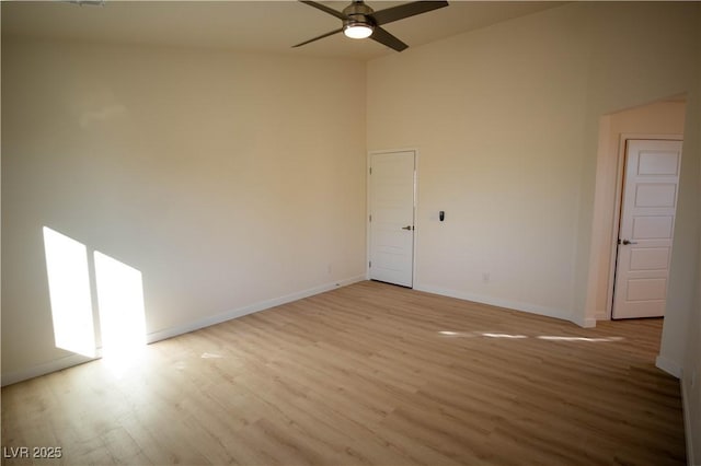 unfurnished room with a ceiling fan, a towering ceiling, light wood-style flooring, and baseboards