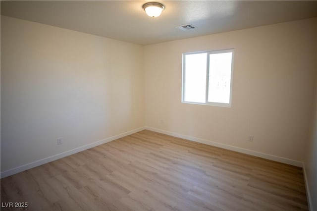 spare room featuring light wood finished floors, visible vents, and baseboards