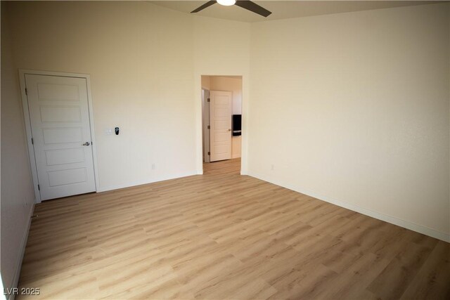 spare room featuring a towering ceiling, light wood-style flooring, baseboards, and a ceiling fan