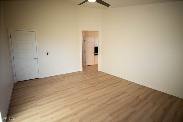 spare room featuring light wood-style flooring, baseboards, a high ceiling, and ceiling fan