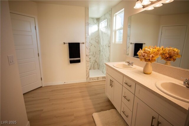 full bath featuring a stall shower, double vanity, a sink, and wood finished floors