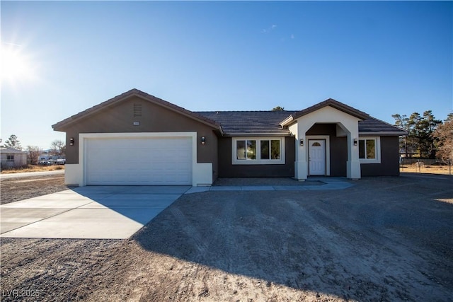 ranch-style home with concrete driveway, a tile roof, an attached garage, and stucco siding