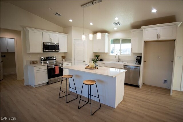 kitchen featuring visible vents, a center island, stainless steel appliances, light countertops, and white cabinetry