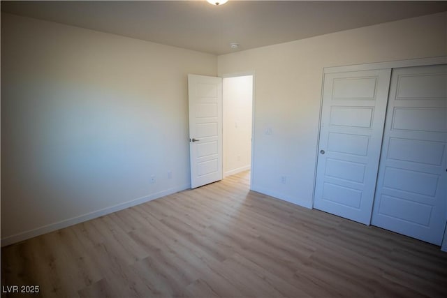 unfurnished bedroom featuring wood finished floors, baseboards, and a closet