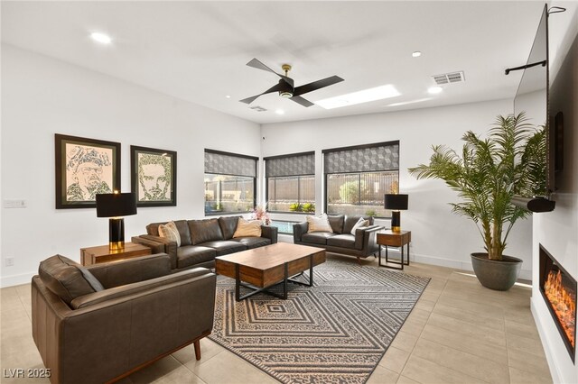 tiled living room with vaulted ceiling with skylight and ceiling fan