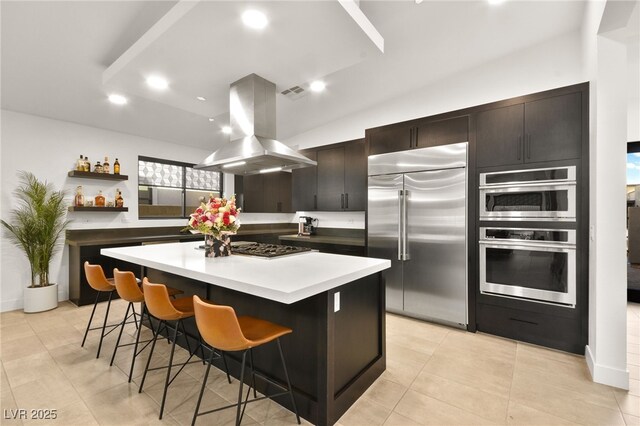 kitchen featuring appliances with stainless steel finishes, a kitchen breakfast bar, island exhaust hood, a center island, and dark brown cabinetry