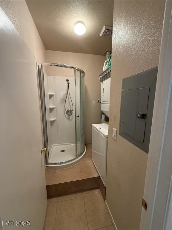 bathroom with stacked washer and clothes dryer, electric panel, walk in shower, tile patterned floors, and a textured ceiling