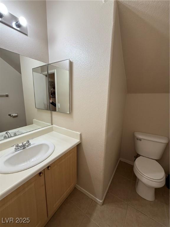 bathroom with tile patterned floors, vanity, toilet, and lofted ceiling