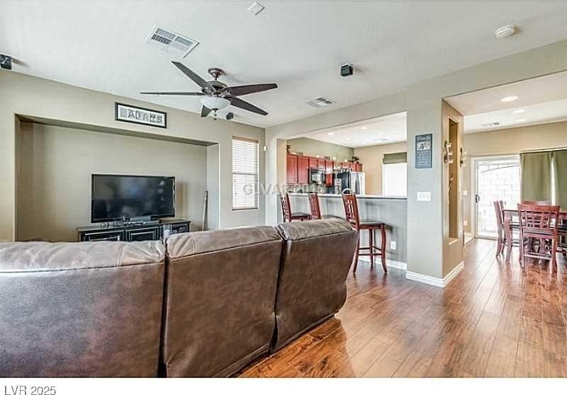 living area with dark wood-type flooring, a ceiling fan, visible vents, and baseboards