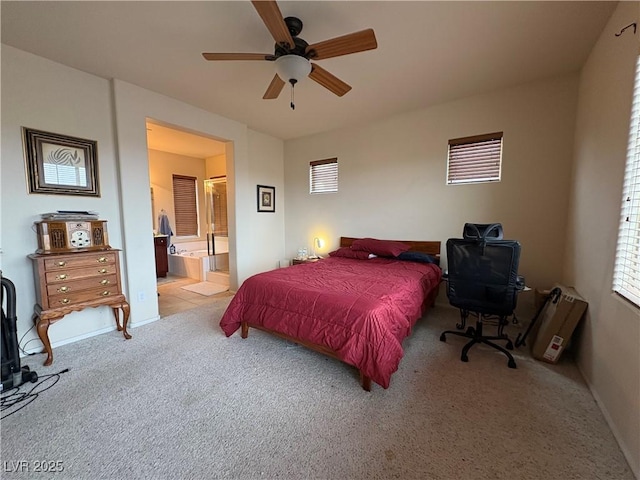 bedroom featuring baseboards, light colored carpet, multiple windows, ensuite bathroom, and a ceiling fan