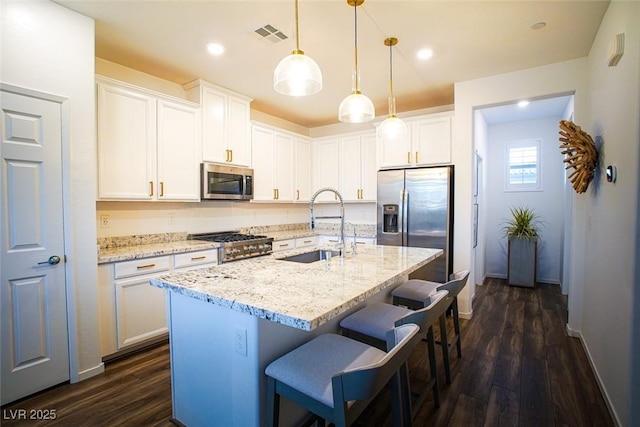 kitchen with sink, stainless steel appliances, white cabinets, and a center island with sink