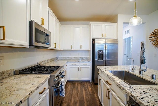 kitchen with appliances with stainless steel finishes, pendant lighting, white cabinets, light stone counters, and dark wood-type flooring