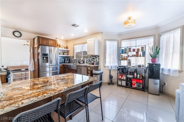 kitchen featuring white cabinetry, stainless steel appliances, tasteful backsplash, light stone countertops, and a healthy amount of sunlight