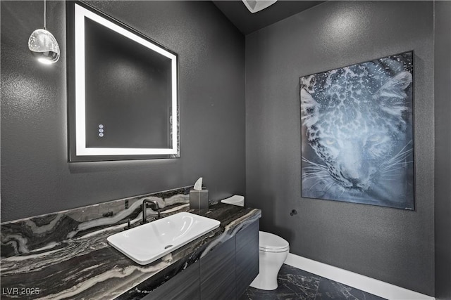 bathroom featuring a textured wall, toilet, vanity, baseboards, and marble finish floor