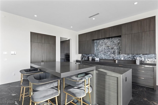 kitchen with visible vents, modern cabinets, marble finish floor, a kitchen bar, and backsplash