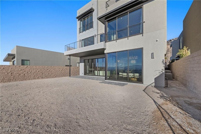 rear view of house featuring fence, a balcony, and stucco siding