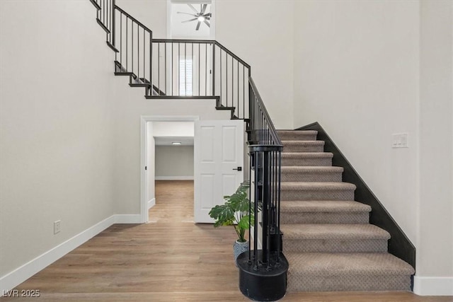 stairway featuring a towering ceiling, wood-type flooring, and ceiling fan