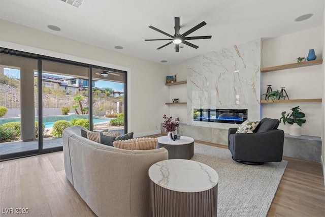 living room featuring a high end fireplace, light hardwood / wood-style flooring, and ceiling fan