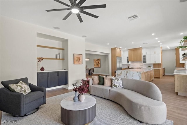 living room featuring ceiling fan, built in features, and light wood-type flooring