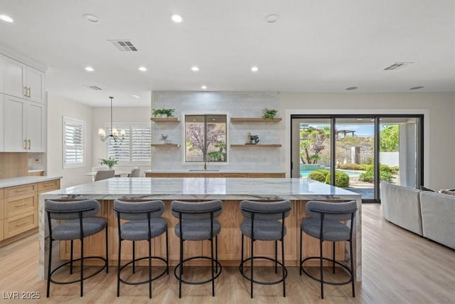 kitchen with a large island, light stone counters, white cabinets, and a kitchen bar