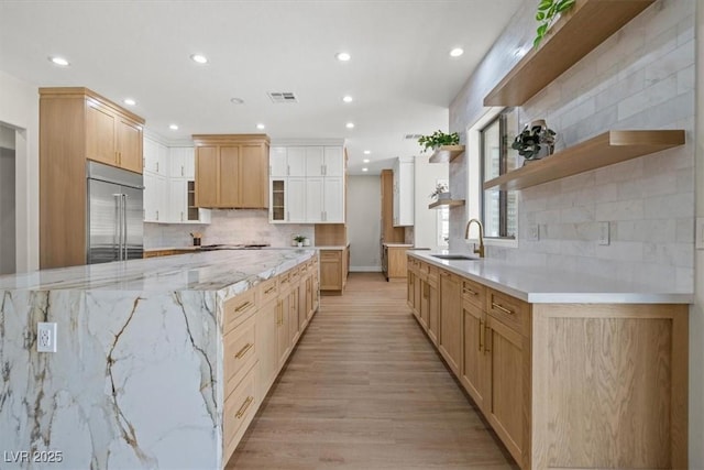 kitchen with light brown cabinetry, stainless steel built in refrigerator, sink, decorative backsplash, and light wood-type flooring