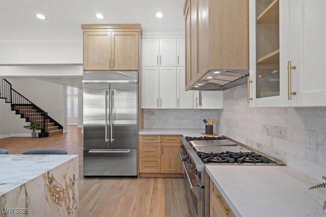 kitchen with backsplash, light hardwood / wood-style floors, high quality appliances, and light brown cabinets