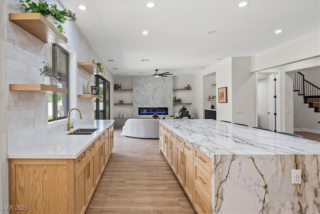 kitchen with sink, a premium fireplace, ceiling fan, light hardwood / wood-style floors, and light brown cabinetry