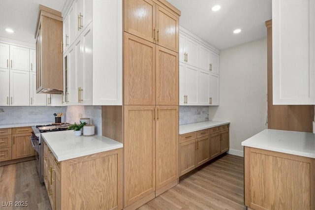 kitchen with tasteful backsplash, light wood-type flooring, white cabinets, and high end range