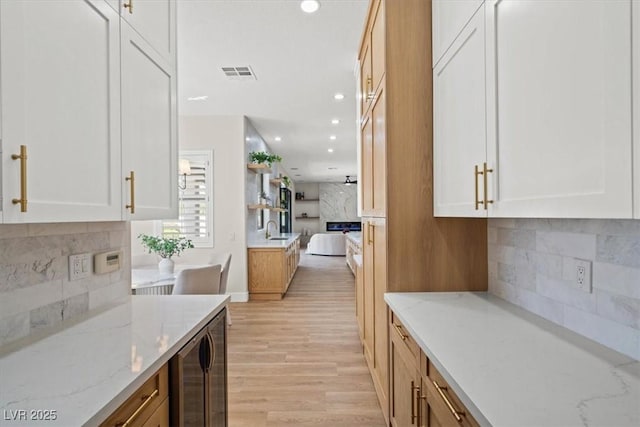 kitchen featuring sink, white cabinetry, light wood-type flooring, light stone countertops, and decorative backsplash