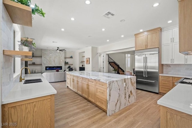 kitchen featuring sink, built in refrigerator, light wood-type flooring, a high end fireplace, and light stone countertops