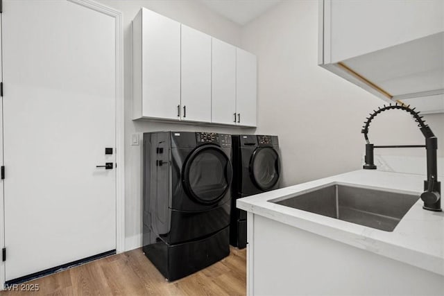 laundry room featuring cabinets, separate washer and dryer, sink, and light hardwood / wood-style floors