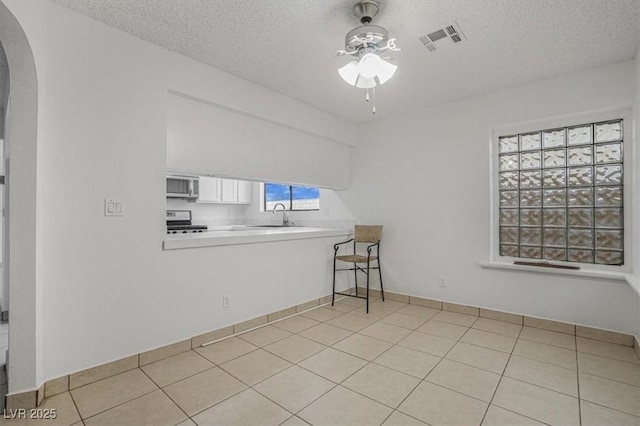 empty room with sink, light tile patterned floors, a textured ceiling, and ceiling fan