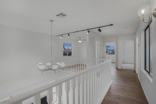 hall with dark hardwood / wood-style flooring, a textured ceiling, and rail lighting